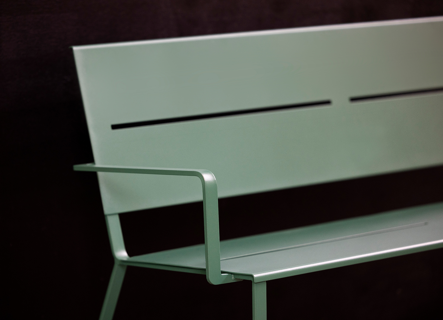 A detail of the armrest on a powder coated, green bench