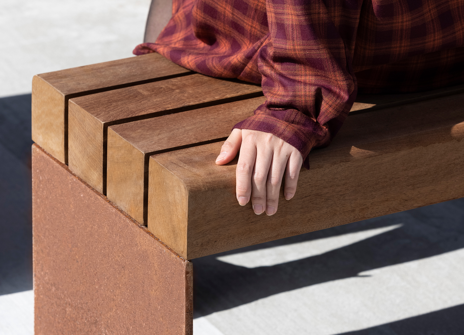 COSI bench in corten steel and mahogany, seen with a hand resting on the seat